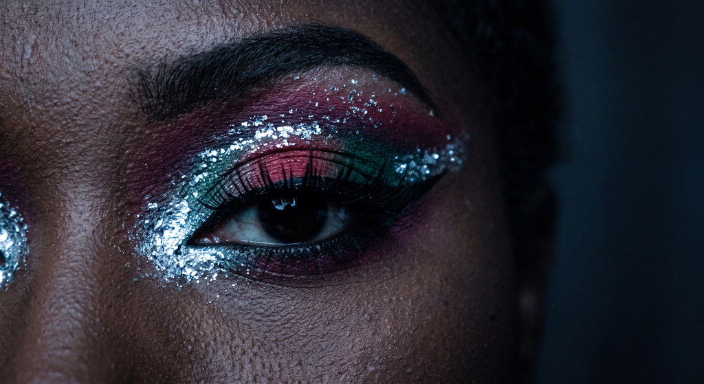 Close-up van één Diepe Winter festivaloog met een gitzwarte grafische wing, een koel edelsteenkleurig verloop van rood, pruim en smaragd, en een ijzige chroomzilveren flits in de binnenste ooghoek, gefotografeerd met dramatische enkelvoudige belichting tegen een bijna zwarte achtergrond