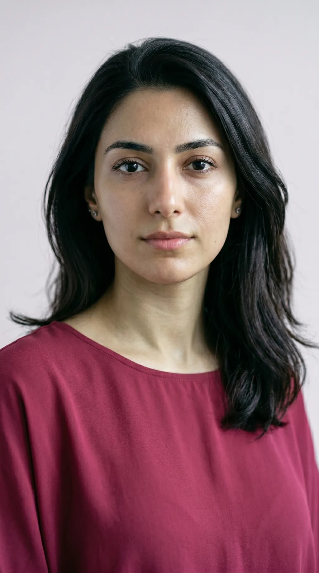 Ongeschminkt portret van een vrouw met koele olijfhuid, een groengrijze zweem over een ondertoon op roze basis, donker haar, tegen een zachtgrijze achtergrond